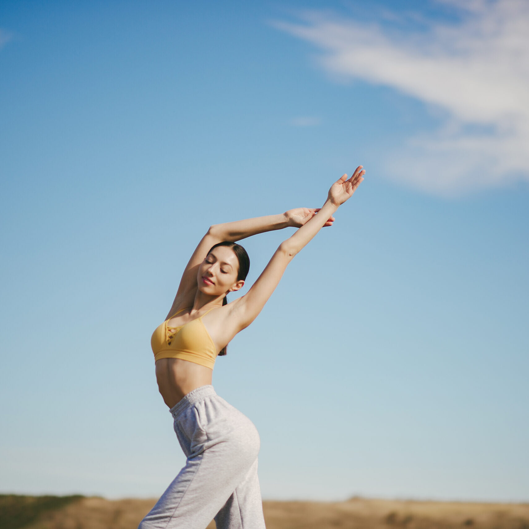 Beautiful girl training on a sky background. Woman in a yellow top. Lady make a yoga